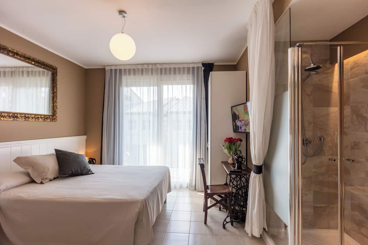 A hotel room with a bed, a desk, a chair, a shower, and a large mirror.