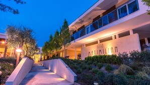 A modern building with a prominent "MAXIMILIAN" sign, a landscaped pathway, and a well-lit entrance area. - Hotel Maximilian (Bardolino)