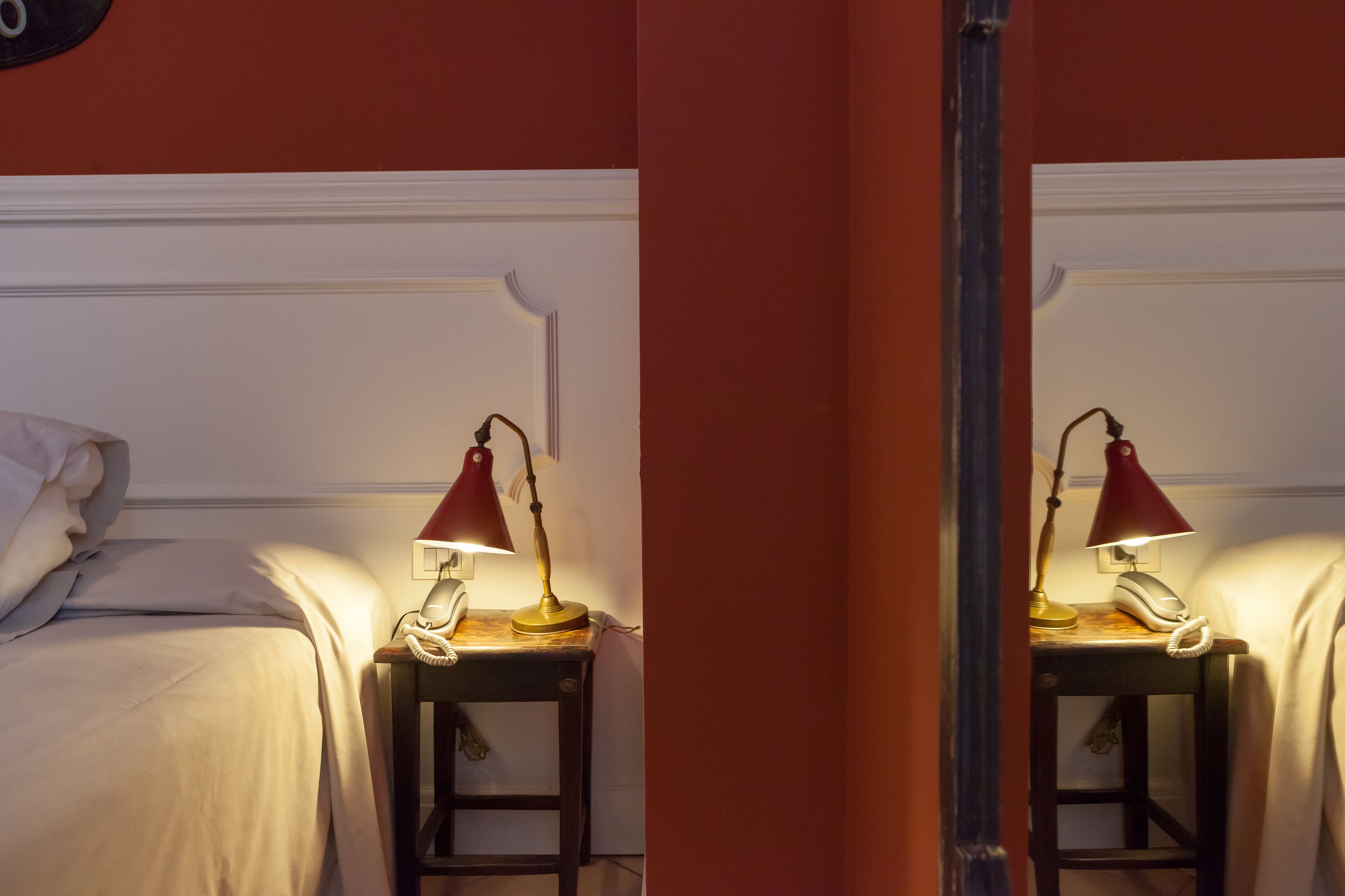 A bed with white bedding, a bedside table with a red lamp, and a telephone.