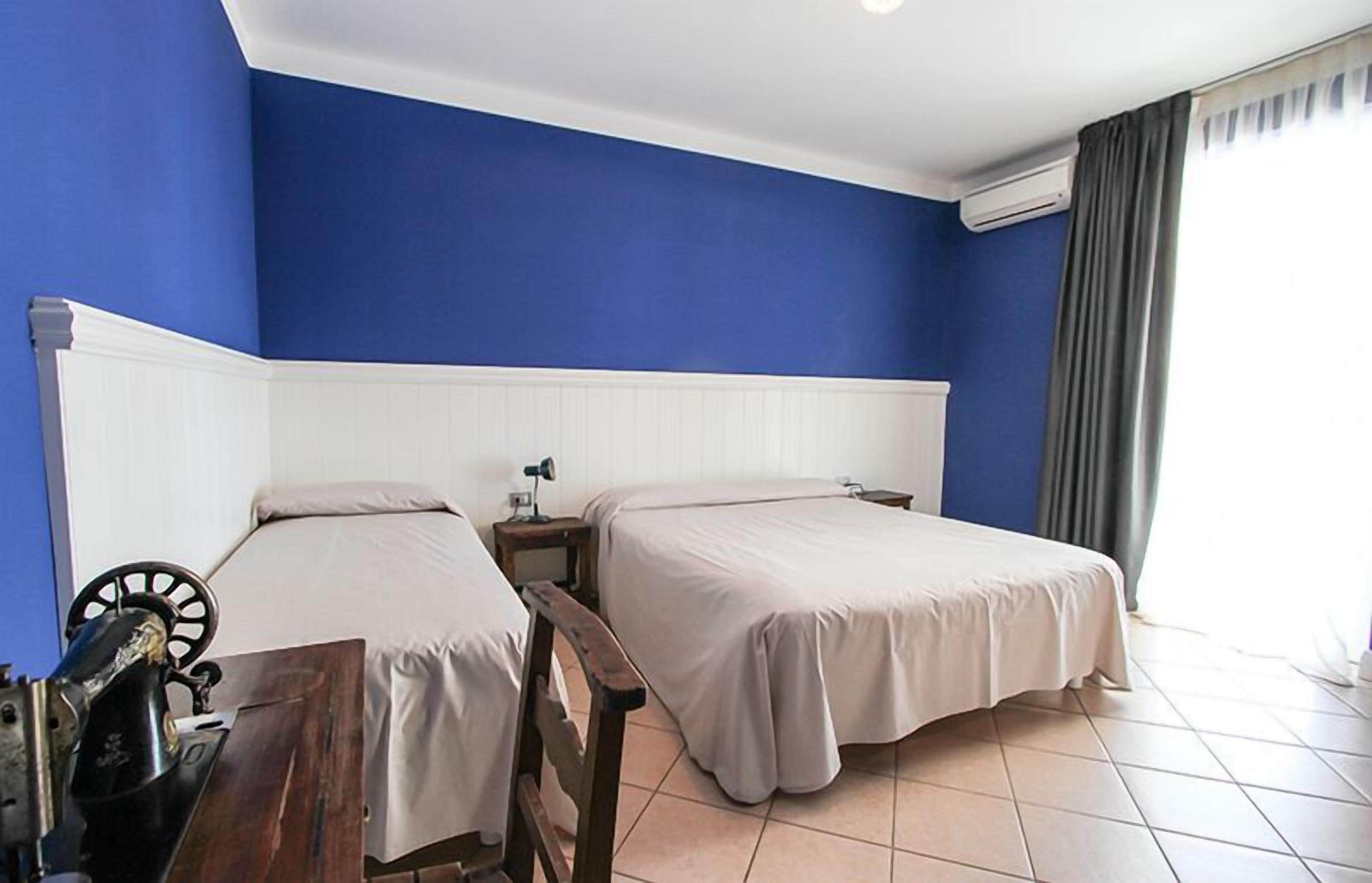 A room with two beds, a wooden bench, a sewing machine, and a window with curtains.