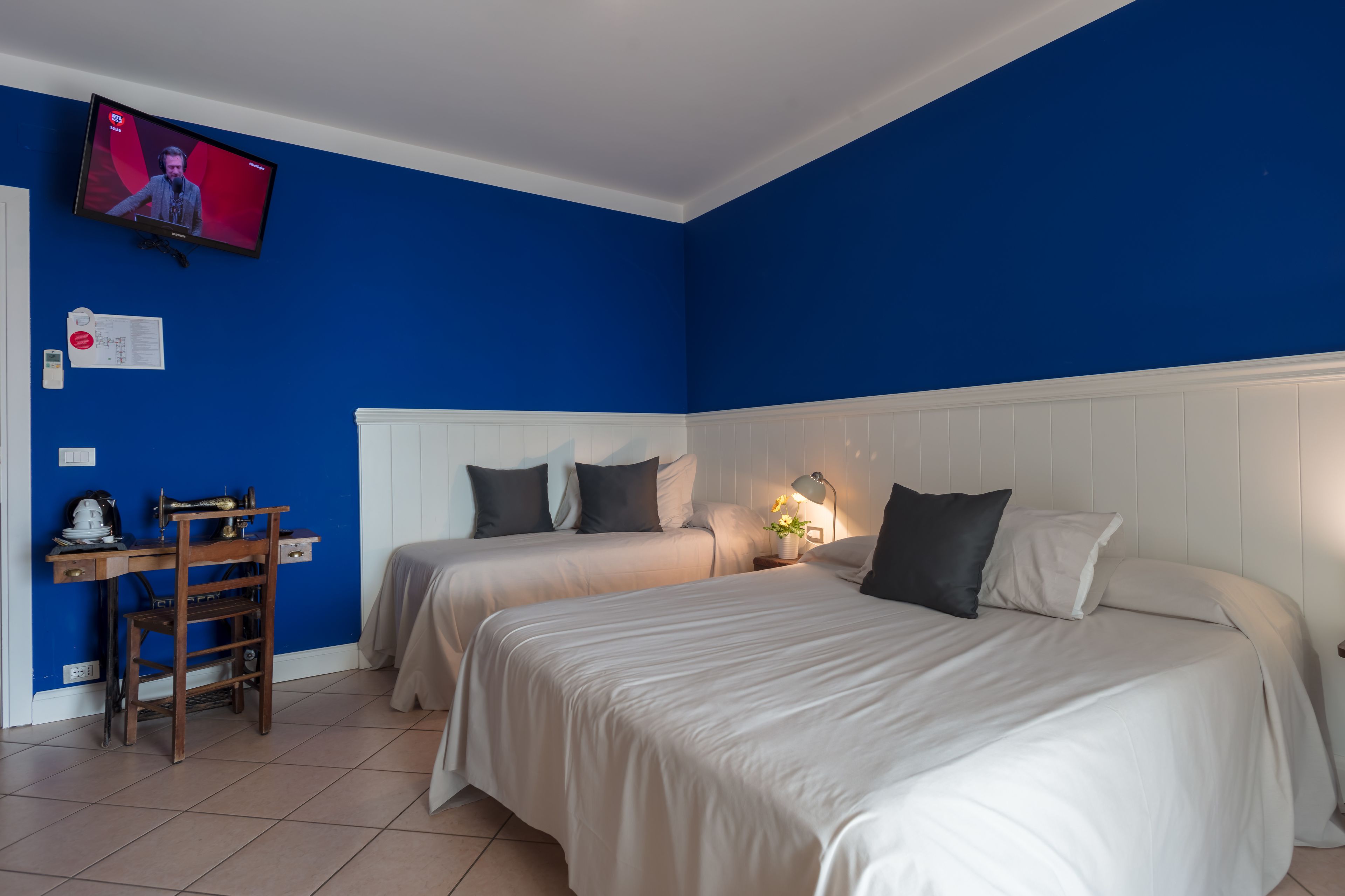 Ein Hotelzimmer mit zwei Betten, einem Schreibtisch und einem an der Wand befestigten Fernseher.