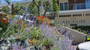 A hotel with a sign reading "MAXIMILIAN HOTEL" surrounded by lush gardens and outdoor seating areas. - Hotel Maximilian (Bardolino)