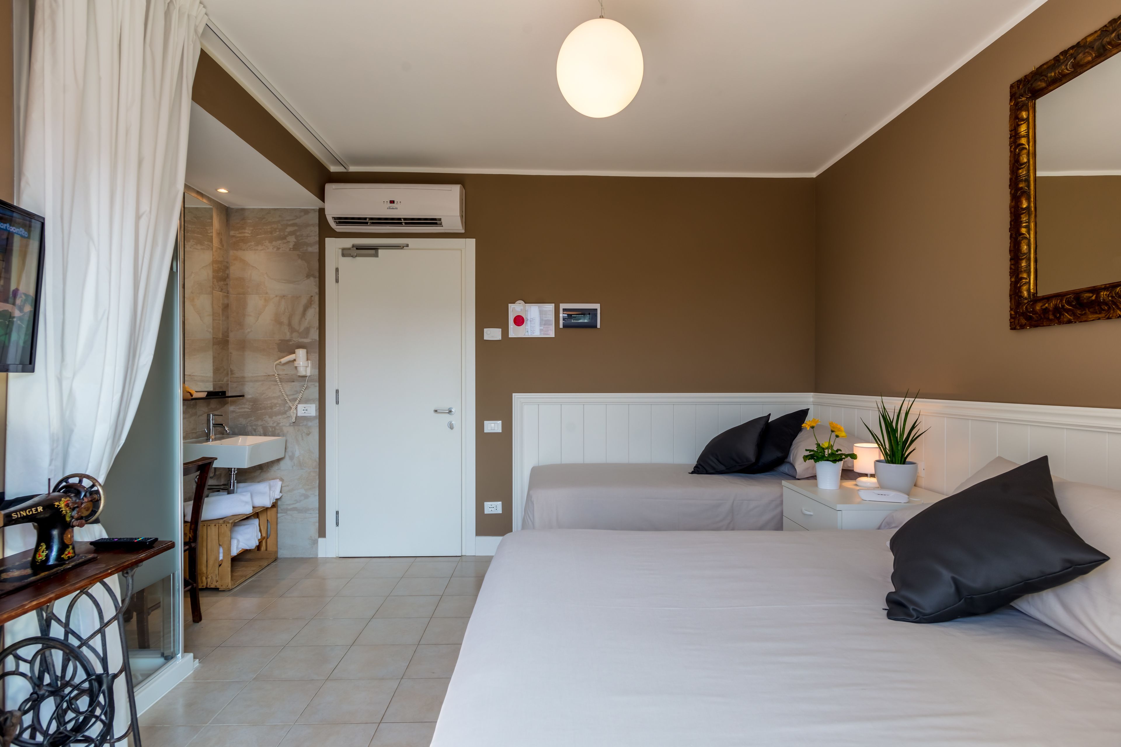 A bedroom with two beds, a bedside table with a lamp, a mirror, and a wall-mounted air conditioner.