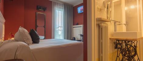 Une chambre d’hôtel avec un lit, une petite table, un radiateur et un téléviseur fixé au mur.