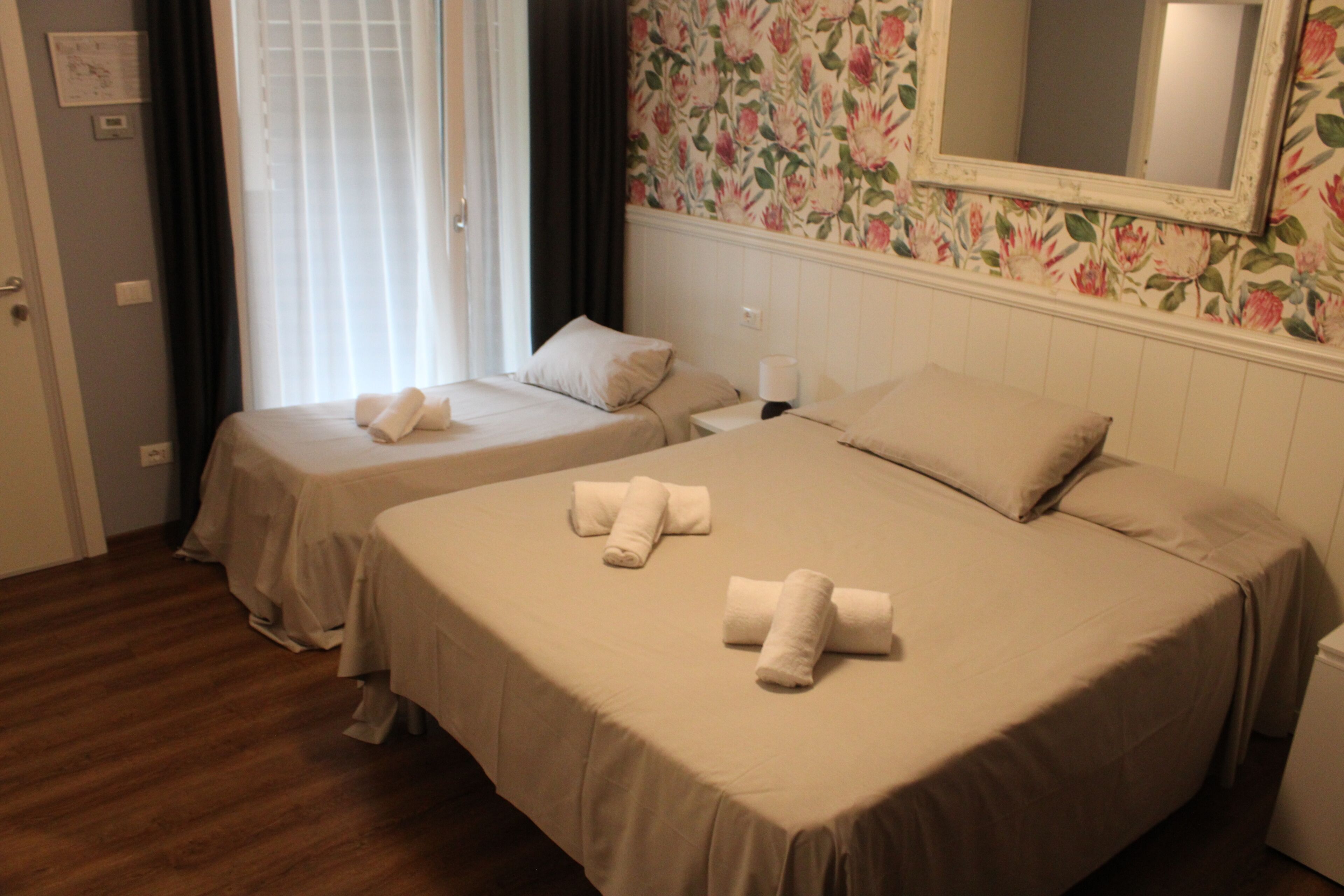 A hotel room with two beds, a mirror, floral wallpaper, and a wooden floor.