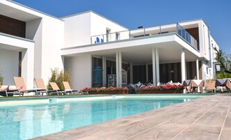 A modern hotel with a pool, lounge chairs, and a covered patio area.