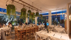 A restaurant with outdoor seating, hanging plants, and large windows. - Hotel Maximilian (Bardolino)