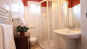 A bathroom with a shower, toilet, sink, and a potted plant.