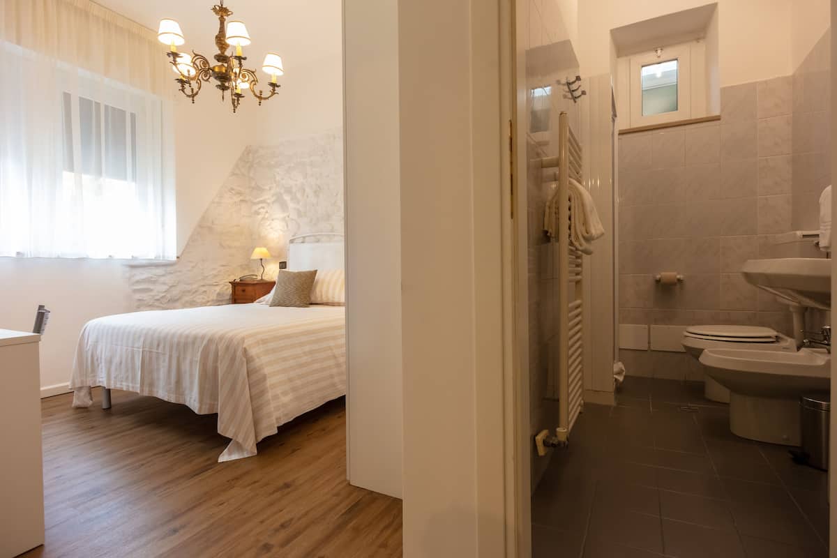 A bedroom with a bed, bedside table, and lamp; a bathroom with a shower, toilet, and sink; and a hallway with a door.