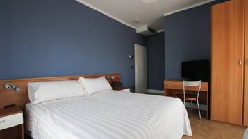 A hotel room with a bed, a desk, a chair, a wardrobe, and a television.