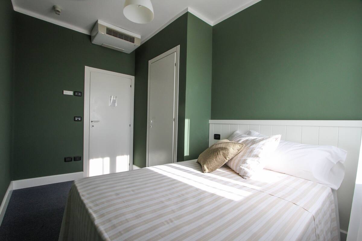 A hotel room with a bed, a white headboard, and a green wall.