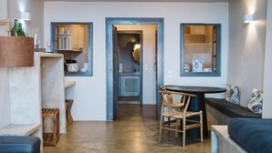 Una sala moderna con un otoman redondo, un sofá azul, una mesa de comedor con sillas y una cocina al fondo.