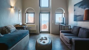 Una sala moderna con un sofá, un reposapiés y un mueble para televisión. Hay ventanas arqueadas y vistas al exterior.