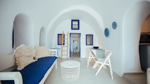 Una habitación moderna y minimalista, con una paleta de colores blanco y azul, que incluye un sofá, una mesa redonda y una escalera que lleva a un nivel superior.