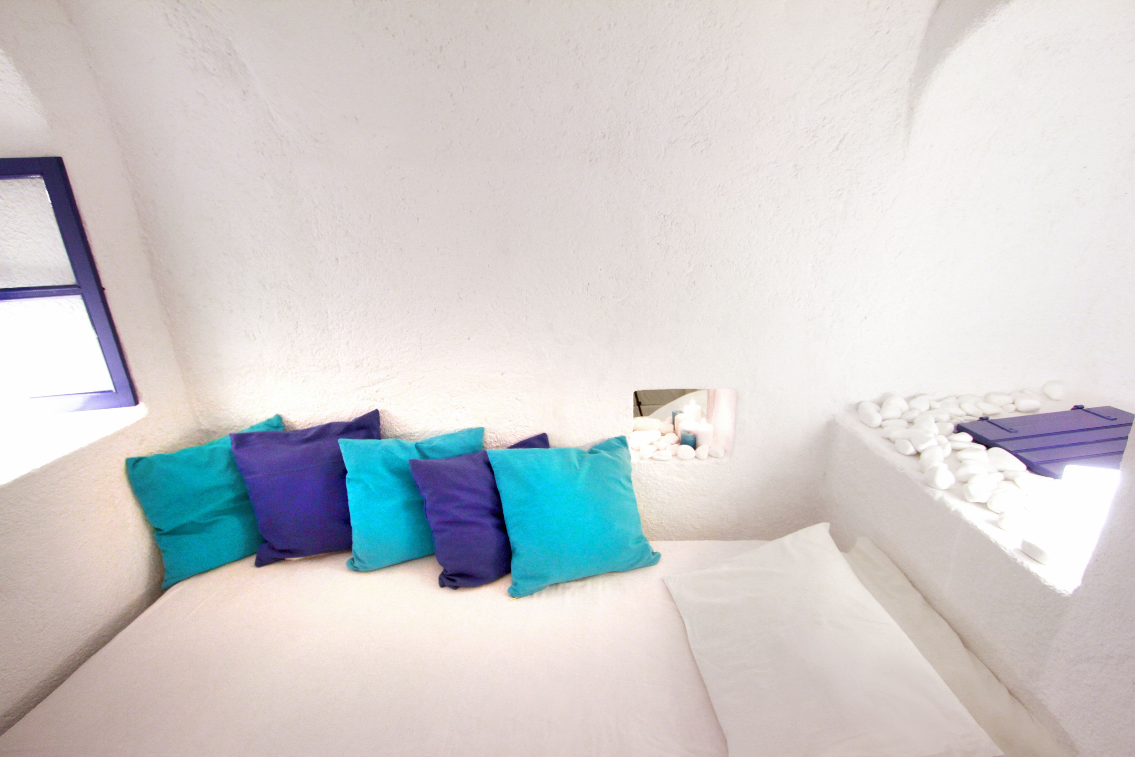 A bedroom with a bed, pillows, a window, and a small shelf with items.