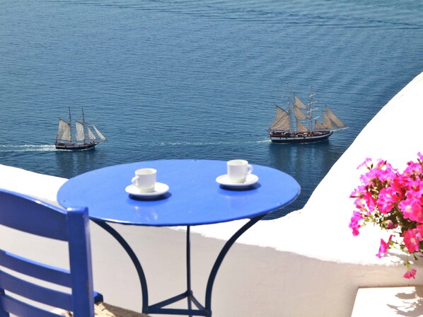 A seaside terrace with a table and chairs, overlooking calm waters with sailboats. - Blu Blanco Cave House by Blu Bianco Vacation Rentals (Santorini)