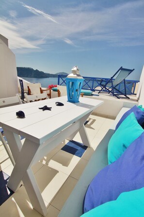 A terrace with a white table, blue and turquoise cushions, and a view of the sea. - Blu Blanco Cave House by Blu Bianco Vacation Rentals (Santorini)