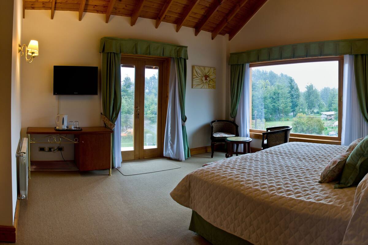A bedroom with a bed, a desk with a chair, a television, and a window with curtains.
