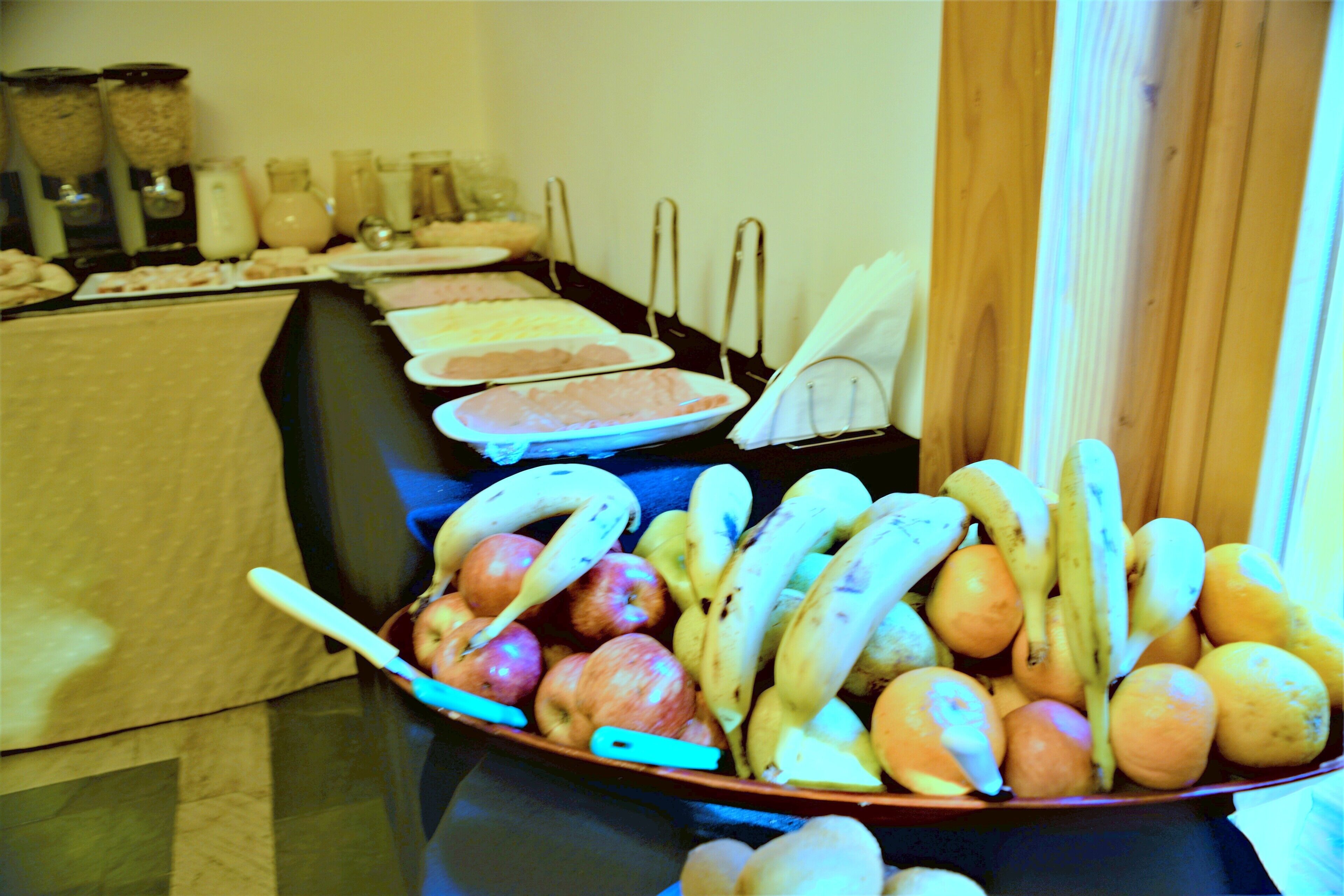 A buffet table with various food items including fruits and a bowl of bananas and apples.