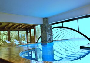 An indoor swimming pool with a stone pillar, wooden deck, and lounge chairs. - Hosteria Patagon (Villa La Angostura)