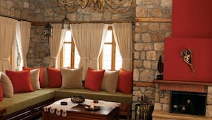 A cozy living room with a stone wall, a fireplace, a sofa with red cushions, and a coffee table.