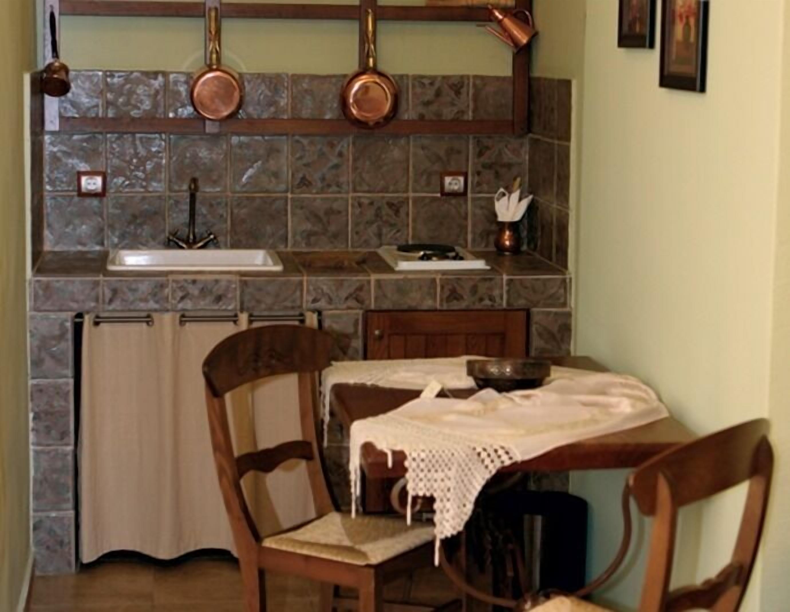 A small kitchen with a sink, a wooden chair, a table with a lace tablecloth, and copper pots hanging above the counter.