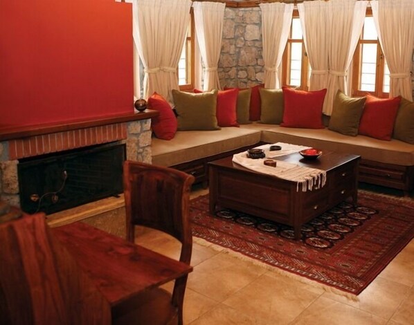 A cozy living room with a stone fireplace, a wooden coffee table, and a red rug. - Roes Suites (Almopia)