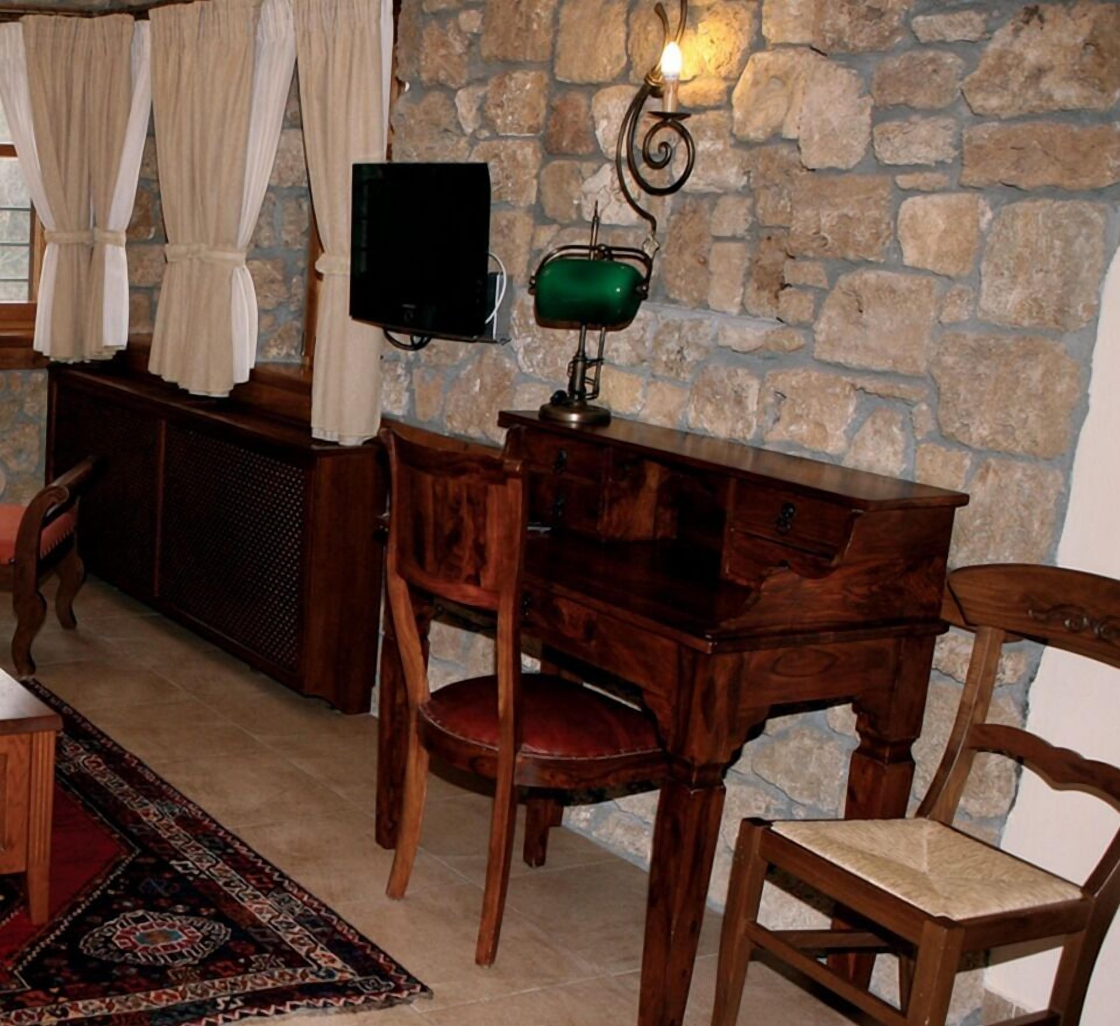 Una habitación con pared de piedra, un escritorio de madera, una silla, un televisor y una lámpara verde.