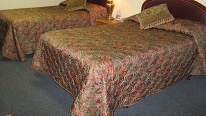 A hotel room with two beds, each with a patterned bedspread and matching pillows. A bedside table with a lamp is between the beds. - Alcoa Inn (Alcoa)