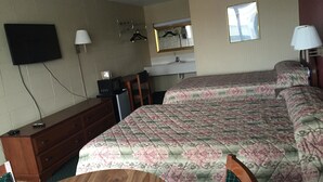 A hotel room with a bed, a desk, a chair, a TV mounted on the wall, and a window. - Alcoa Inn (Alcoa)