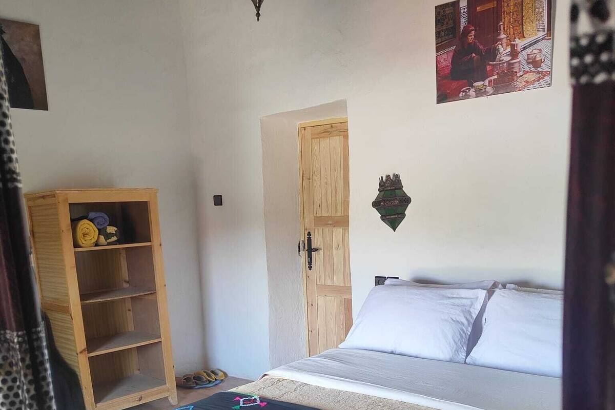 Quarto com cama, guarda-roupa de madeira, porta e um objeto decorativo na parede.