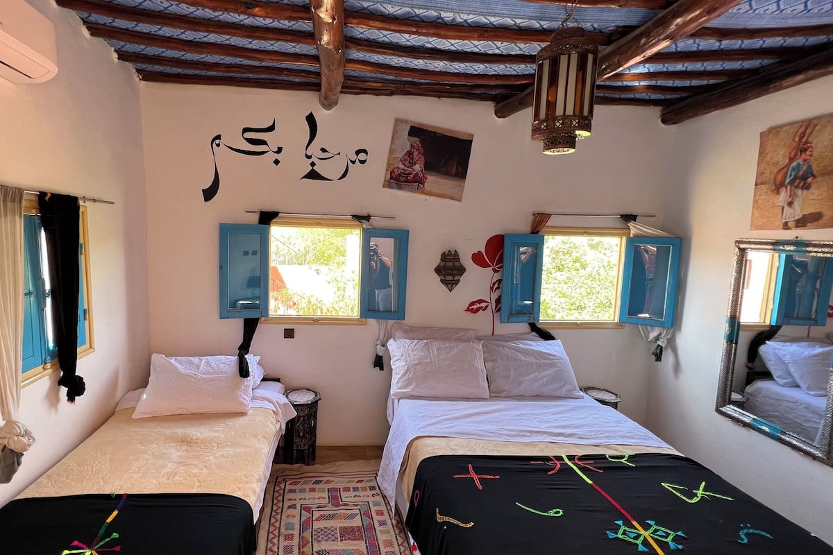 Quarto com duas camas, janela e ar-condicionado fixado na parede.