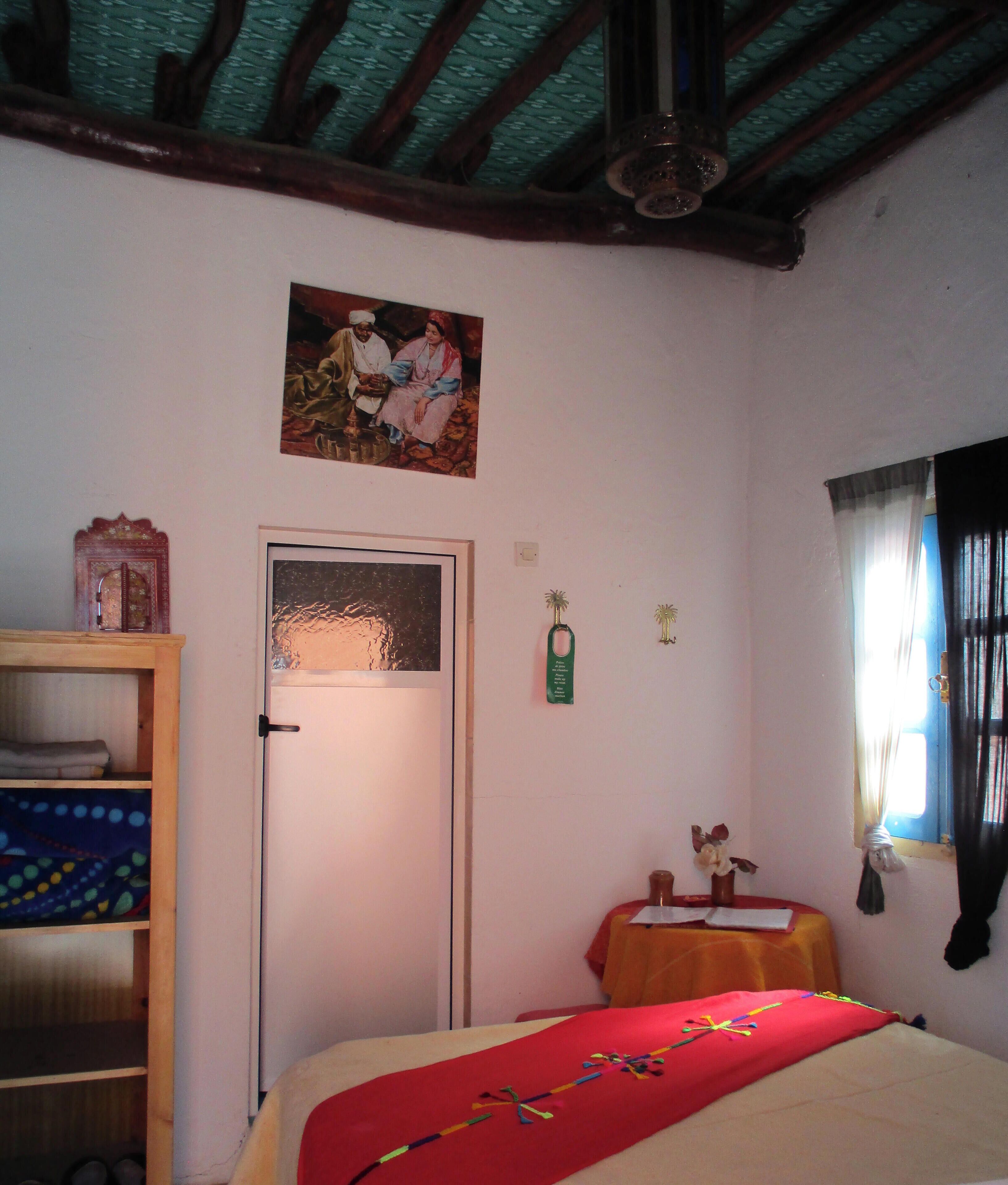 Ein Schlafzimmer mit einem Bett, einem Holzschrank, einer Tür, einem gerahmten Bild an der Wand und einem kleinen Tisch mit Tischdecke.