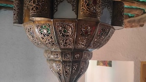 Un detallado y ornamentado farol de metal colgando del techo, decorado con patrones intrincados y un diseño geométrico.