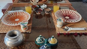 Una mesa de comedor preparada con platos, vasos y aderezos en un salón con un sofá y cojines.