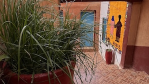 Un estrecho callejón con una planta en maceta al frente, un mural en la pared y un edificio con puerta azul al fondo.