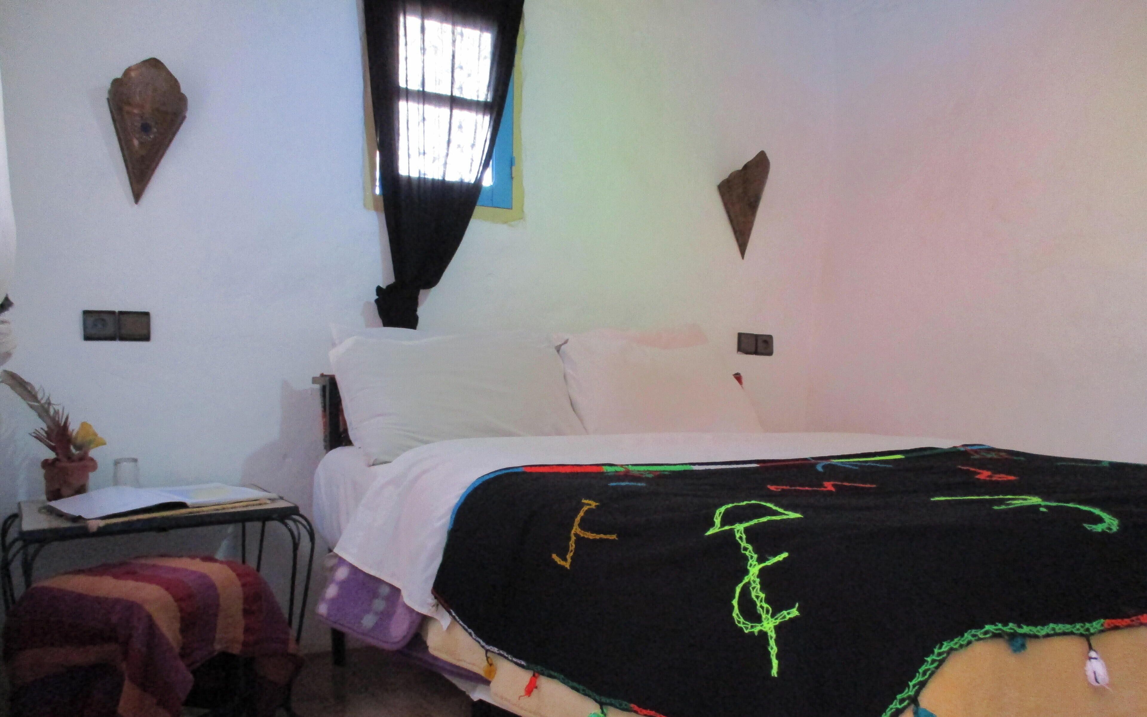 Een slaapkamer met een bed, een klein tafeltje met een plant en een raam met gordijnen.