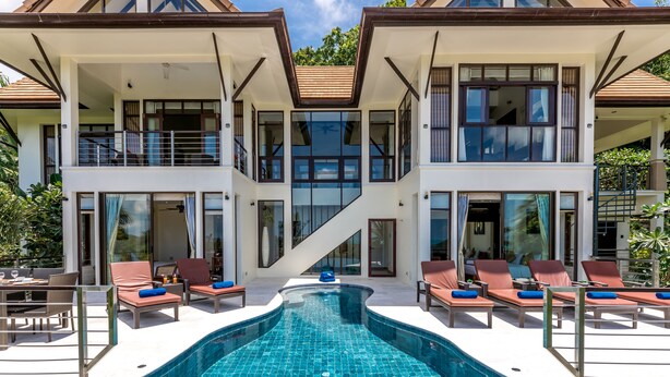 Una casa moderna de dos pisos con piscina, sillones de descanso y una escalera que sube al piso superior.