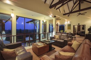 A spacious living room with leather sofas, a coffee table, and large windows offering a view of the outdoors. - Villa Maphraaw (Koh Samui)