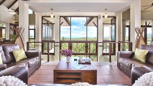 Un amplio salón con sofás de cuero, una mesa de centro y grandes ventanas con vistas al exterior.