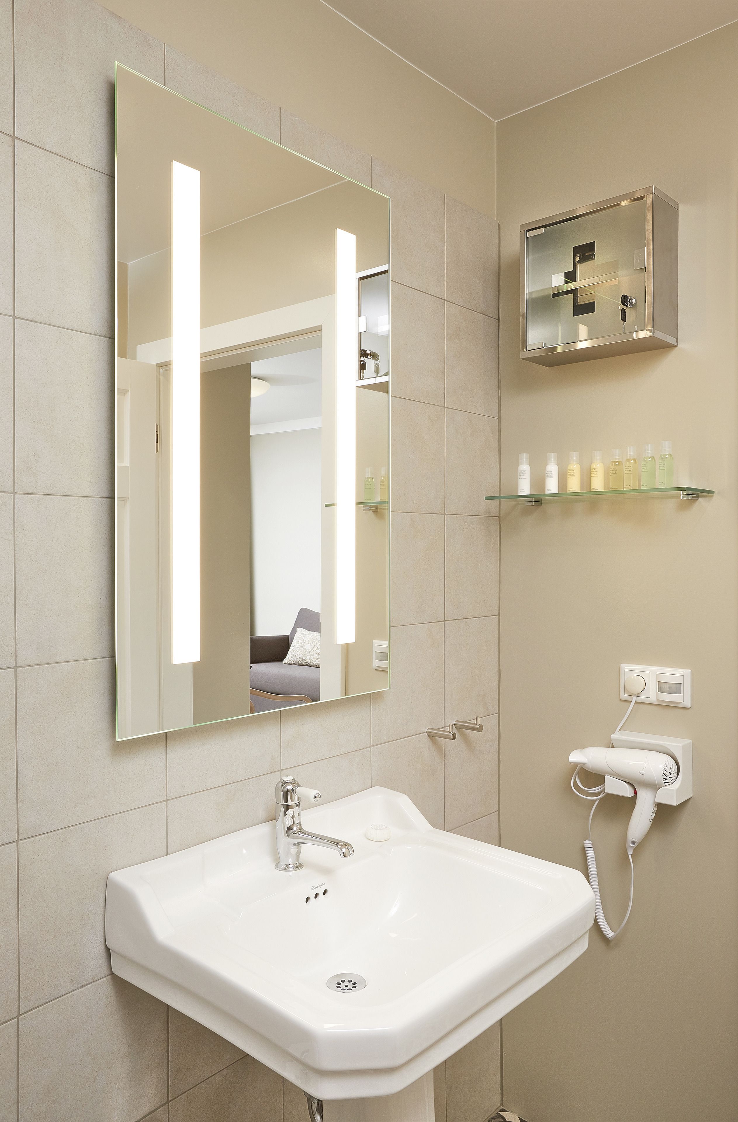 A bathroom with a large mirror, a sink, a hairdryer, and a shelf with toiletries.