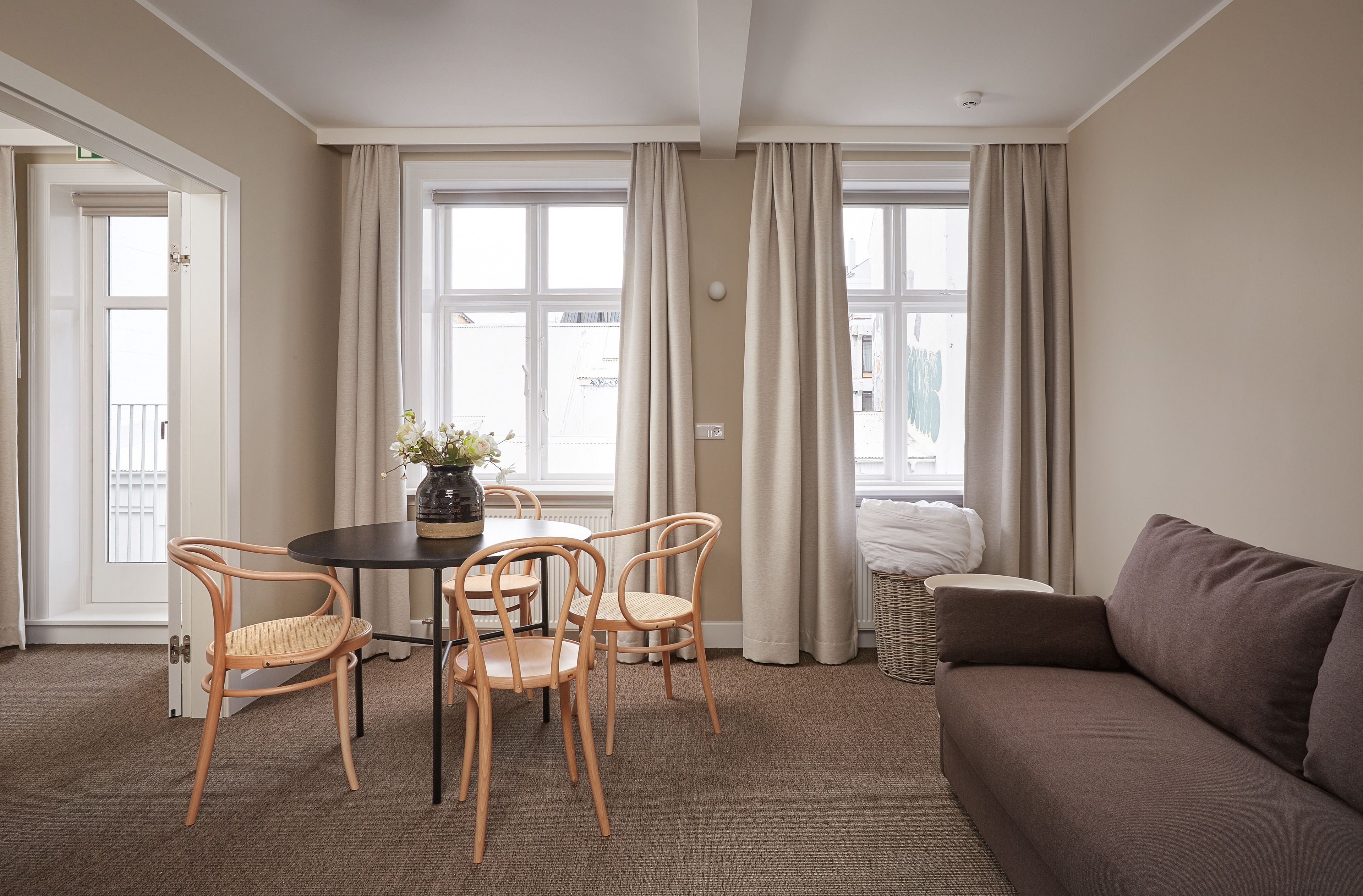 Una habitación con una mesa redonda, cuatro sillas, un sofá y ventanas grandes con cortinas.