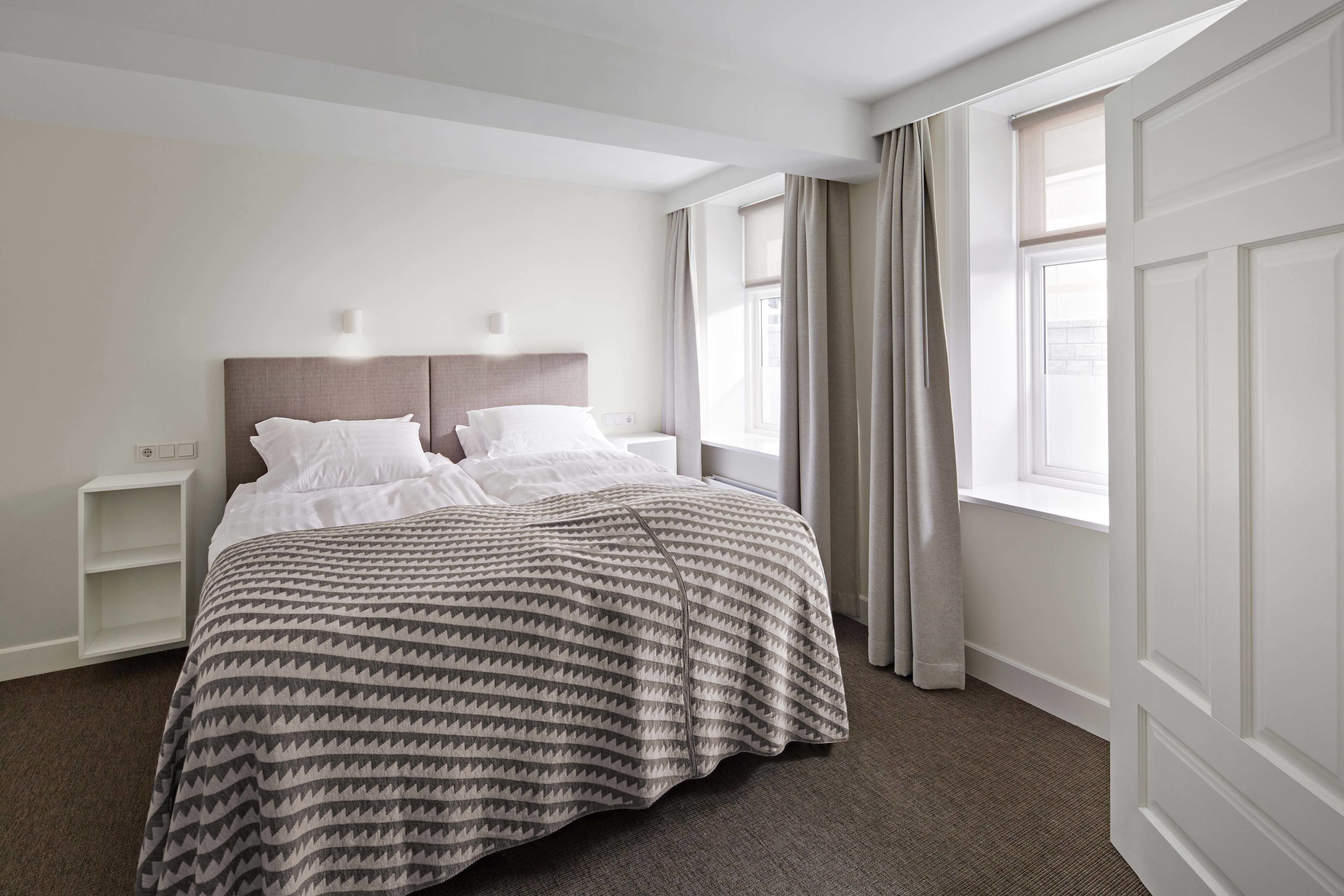 A neatly made bed with a patterned bedspread, a bedside table, and a window with curtains.