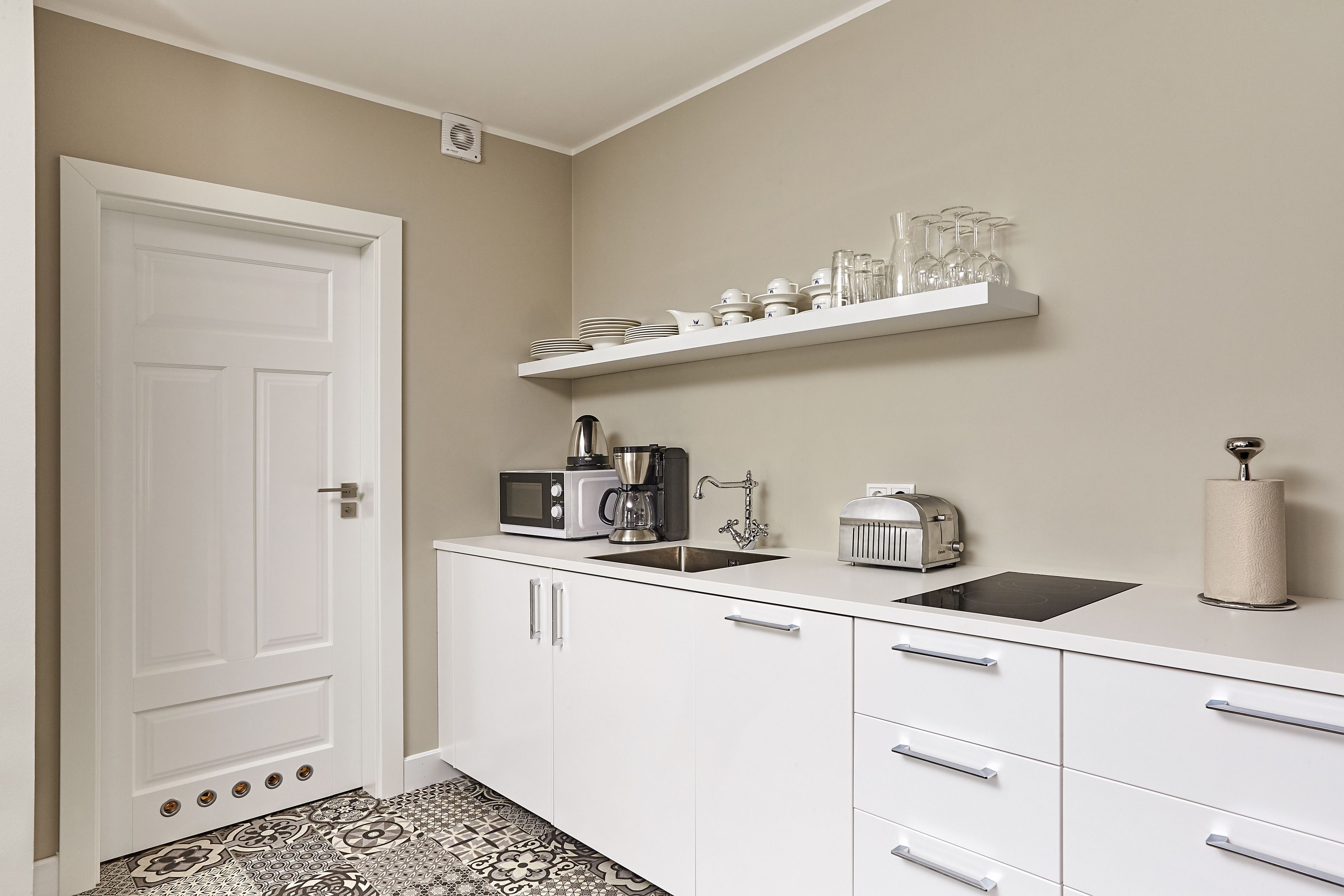 A kitchen with white cabinets, a microwave, a toaster, a sink, and a shelf with glassware.