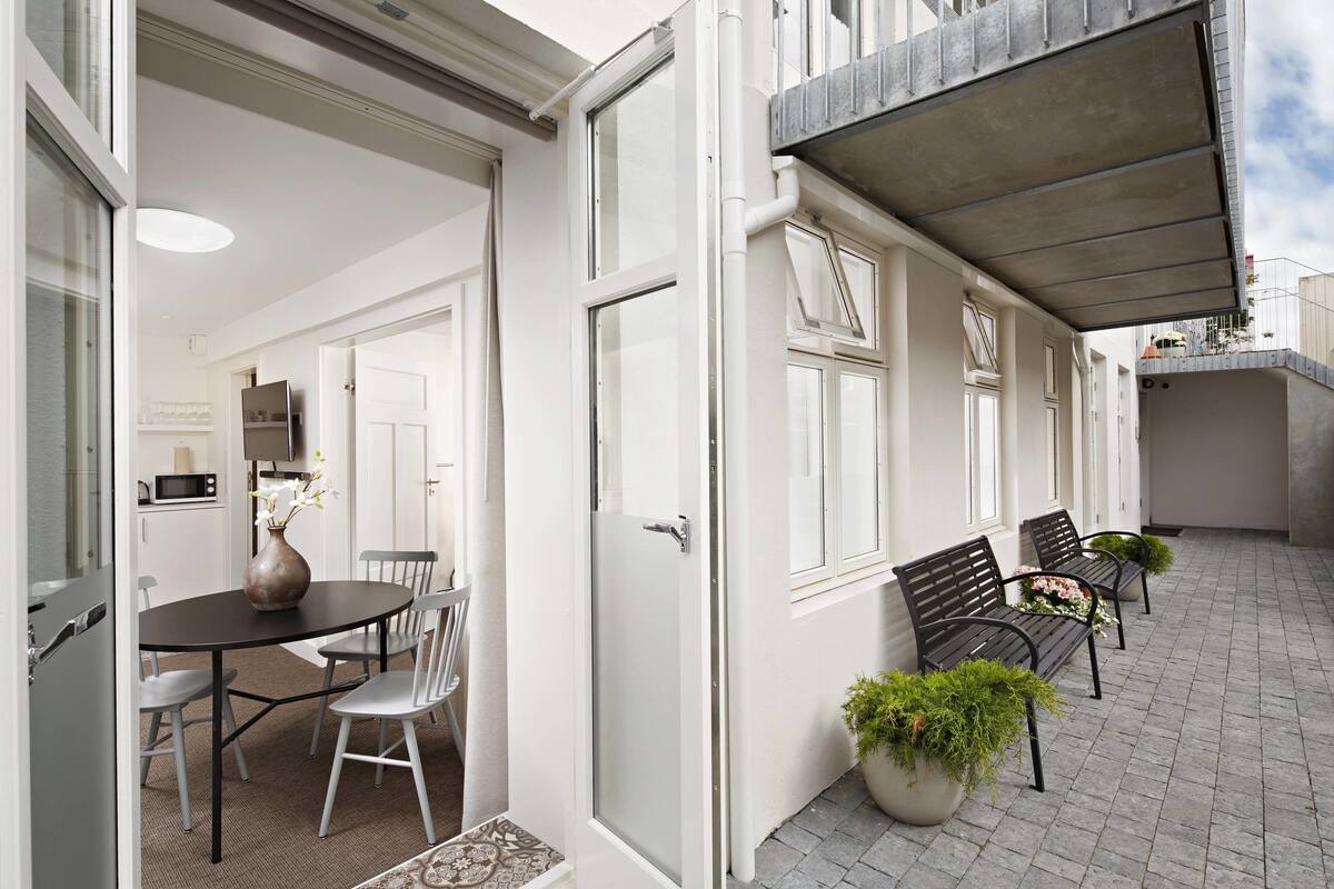 An open door leading to a dining area with a table and chairs, a potted plant, and a bench outside.