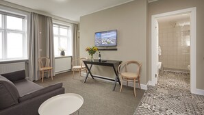 A modern hotel room with a grey sofa, a small round table, a TV on the wall, and a shower area visible through an open door. - Ice Apartments Reykjavik by Heimaleiga (Reykjavik)