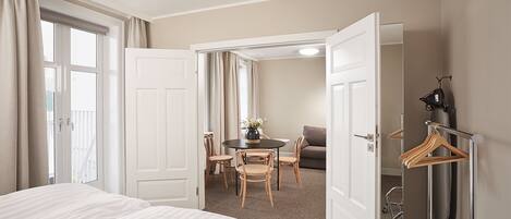 A hotel room with a bed, a dining table with chairs, a small sofa, and a coat rack.