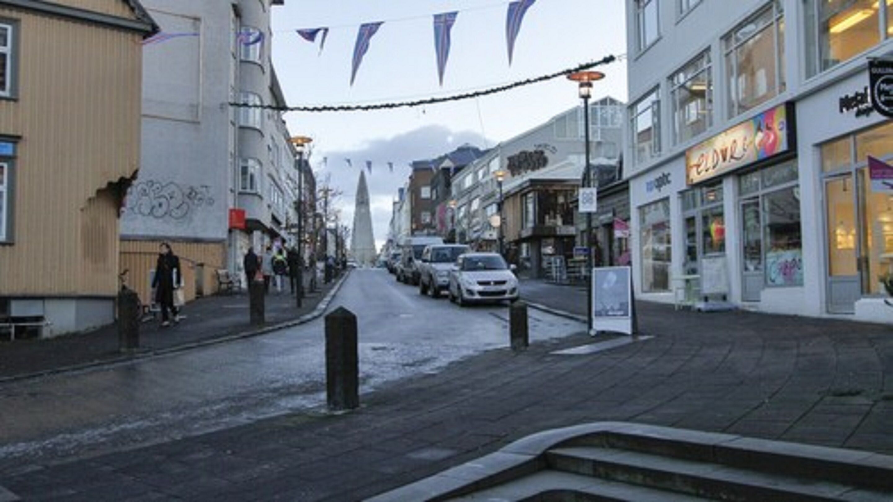 Une vue de rue avec des immeubles, des boutiques et des voitures garées.