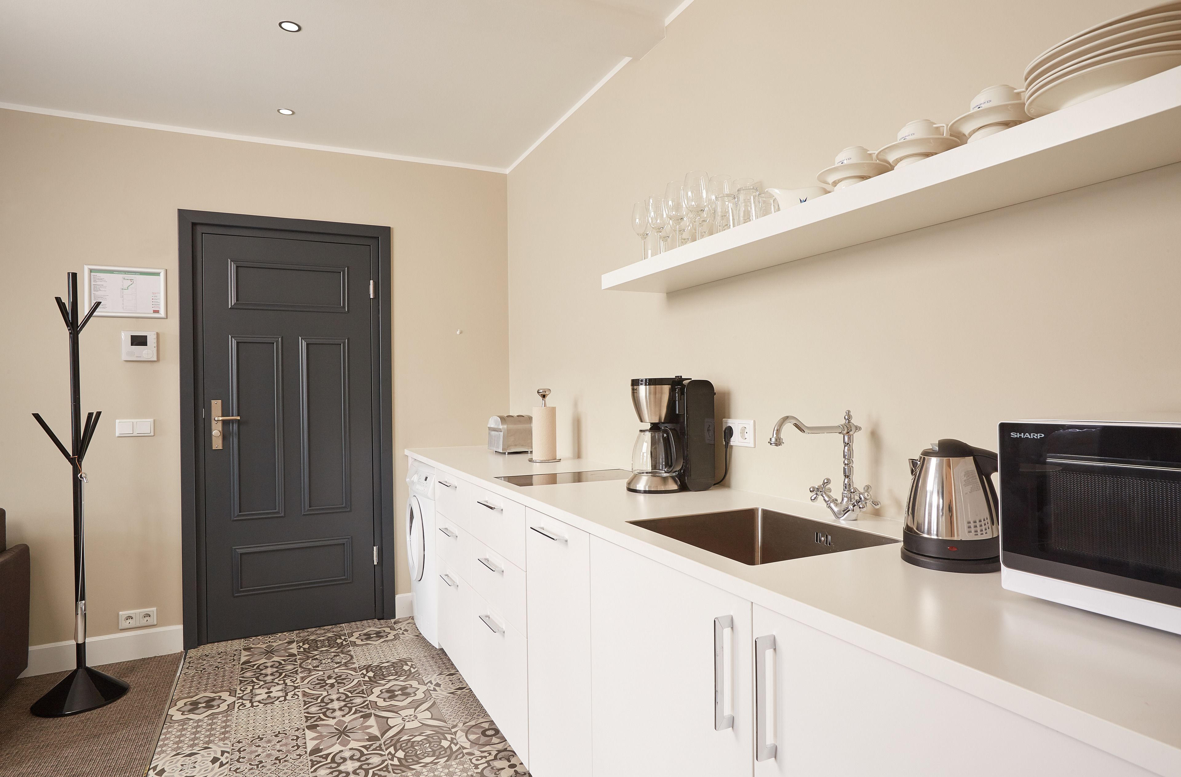 A modern kitchen with white cabinetry, a built-in microwave, a coffee maker, and a shelf with glasses.