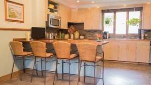 Una cocina con una isla central, cuatro sillas de mimbre, un microondas y armarios de madera.